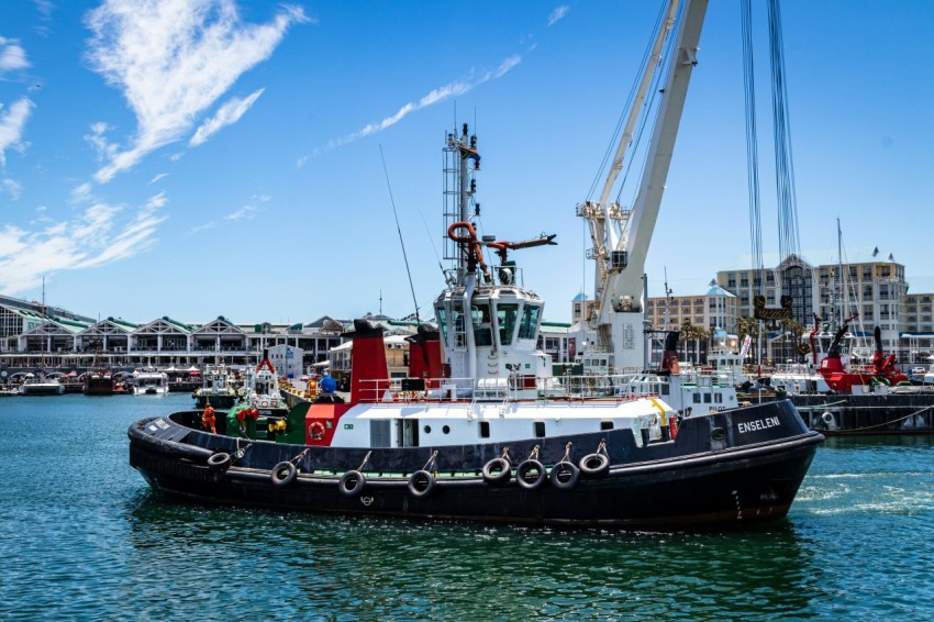 tug boat by quay crane and near buildings at daytime