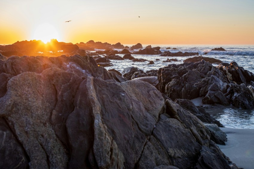 the sun is setting over a rocky beach