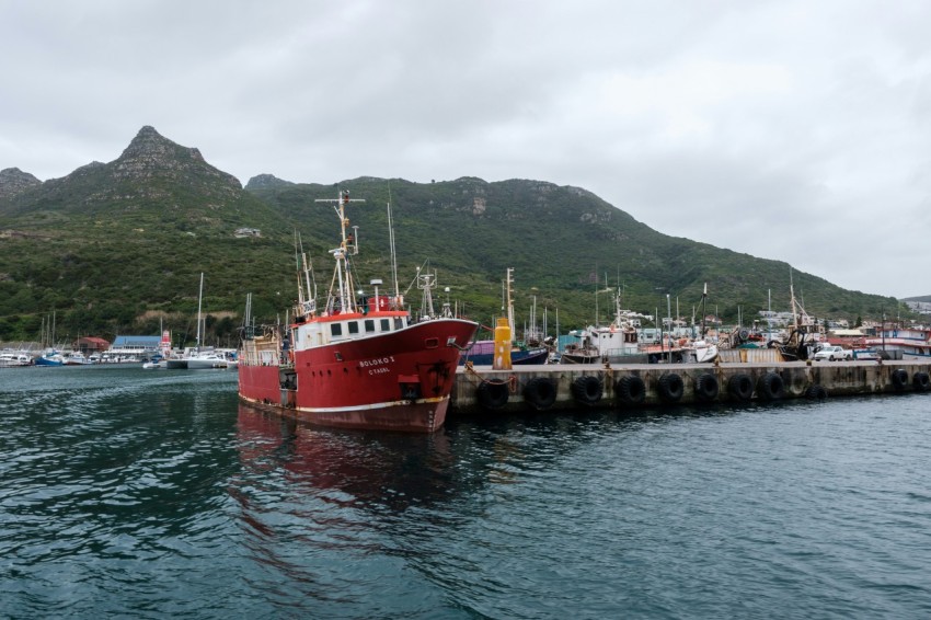 a red and white boat in the water by a dock with mountains in the background