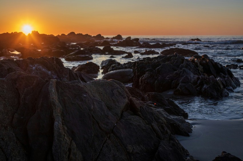 the sun is setting over the ocean and rocks