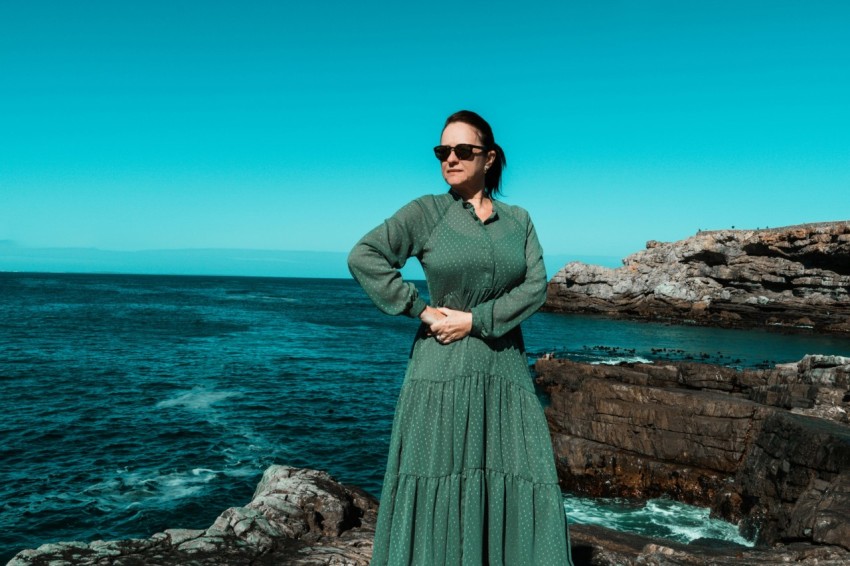 woman in green long sleeve dress standing on rock formation near sea during daytime 0gR