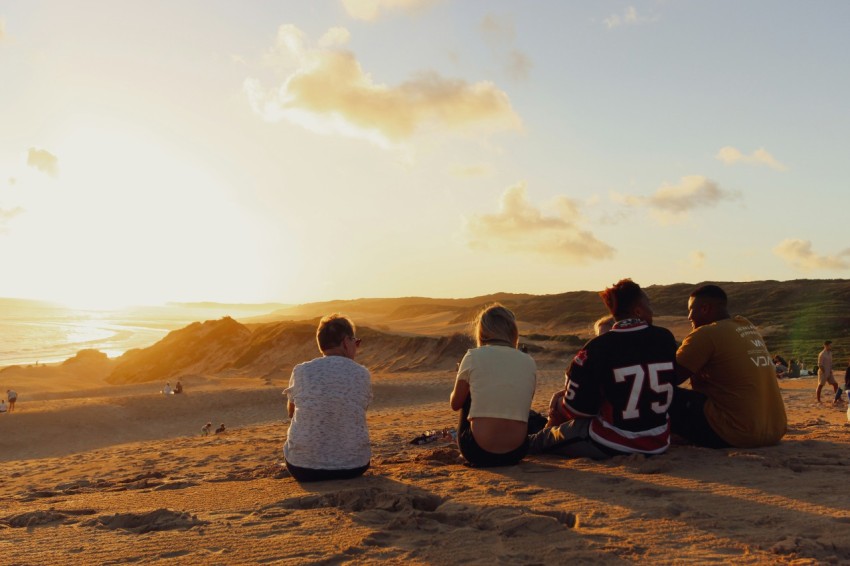 a group of people sitting on top of a sandy beach sZdVWNU e