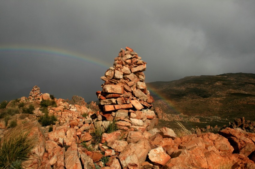 a pile of rocks with a rainbow in the background Yn