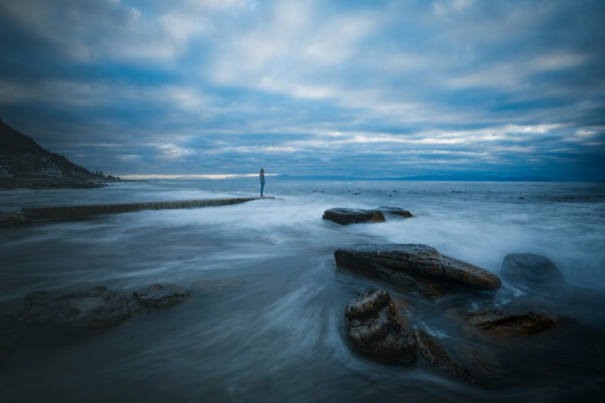 person standing on rock formation on sea under blue sky during daytime 6