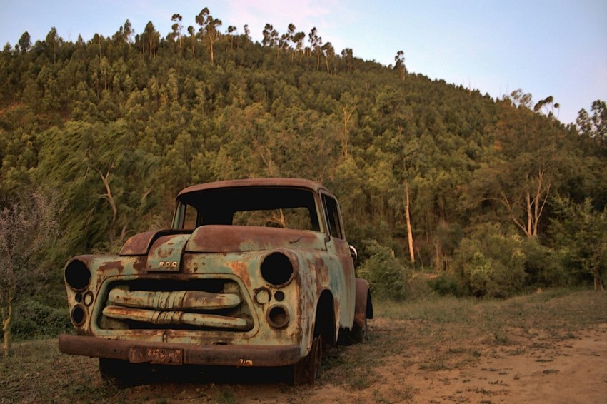 an old rusted out truck sitting in a field