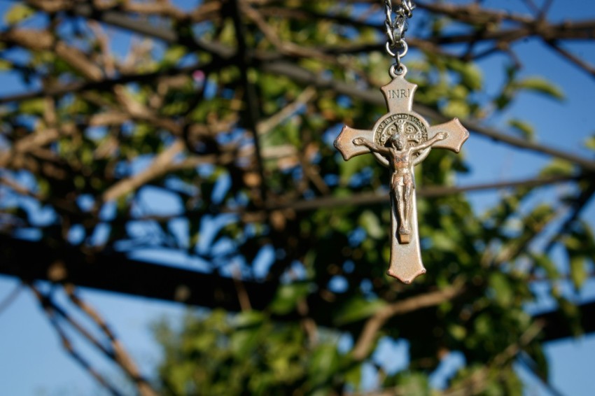 a cross hanging from a chain in front of a tree WcNTK