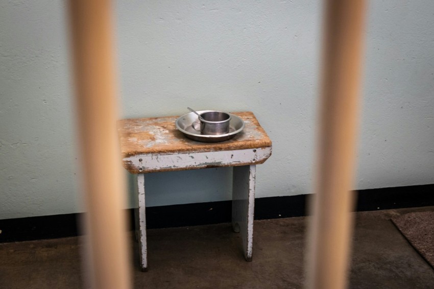 stainless steel cup on plate at stool seat by wall behind metal bars