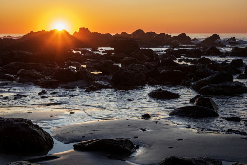 the sun is setting over a rocky beach