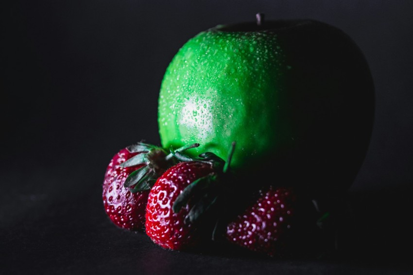 green apple with strawberries on black surface acp