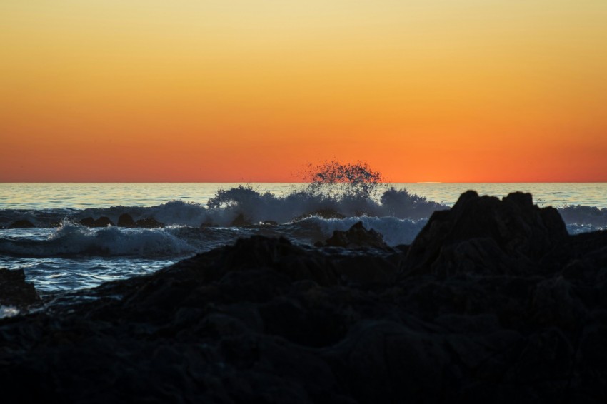 the sun is setting over the ocean and rocks