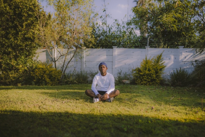 man in white crew neck t shirt sitting on green grass field during daytime