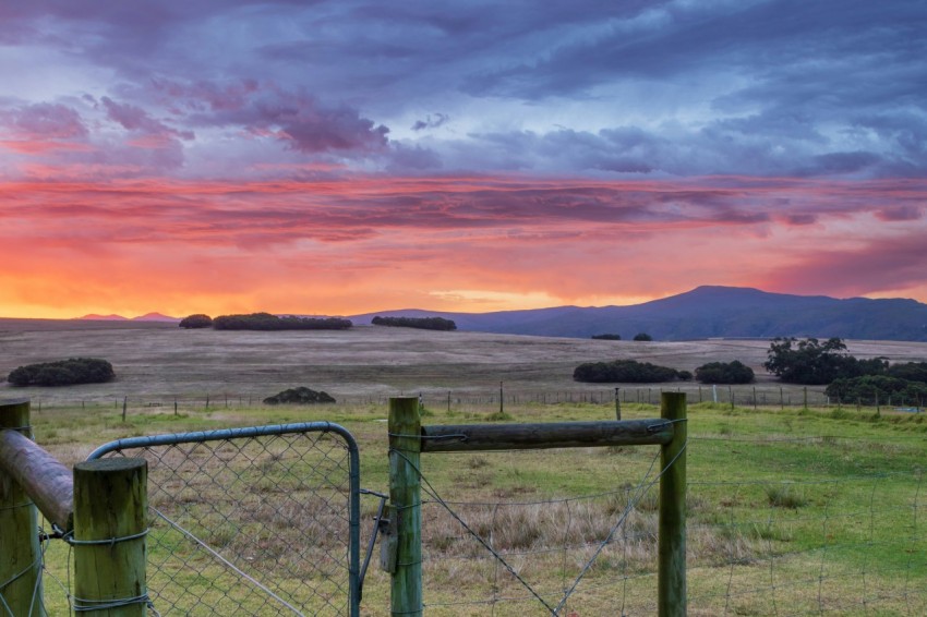 a fence in a field with a sunset in the background