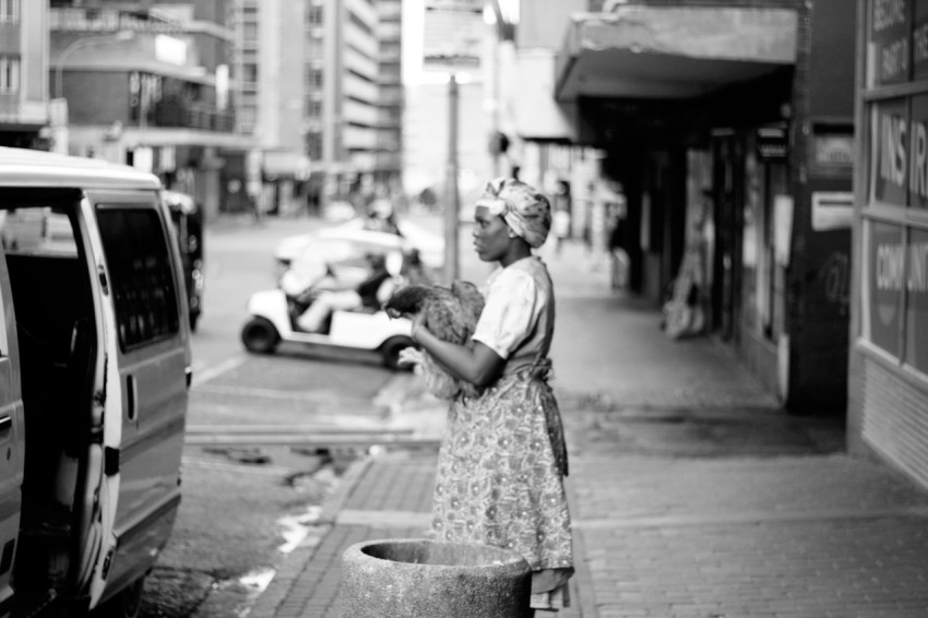 grayscale photo of woman in dress standing on sidewalk