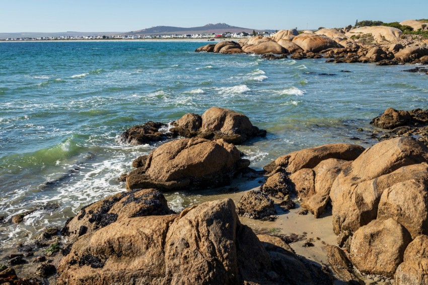 a rocky beach with a body of water and a bridge in the distance ZMslz