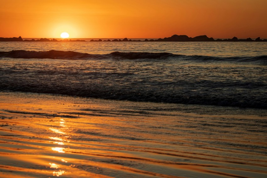 the sun is setting over the water at the beach