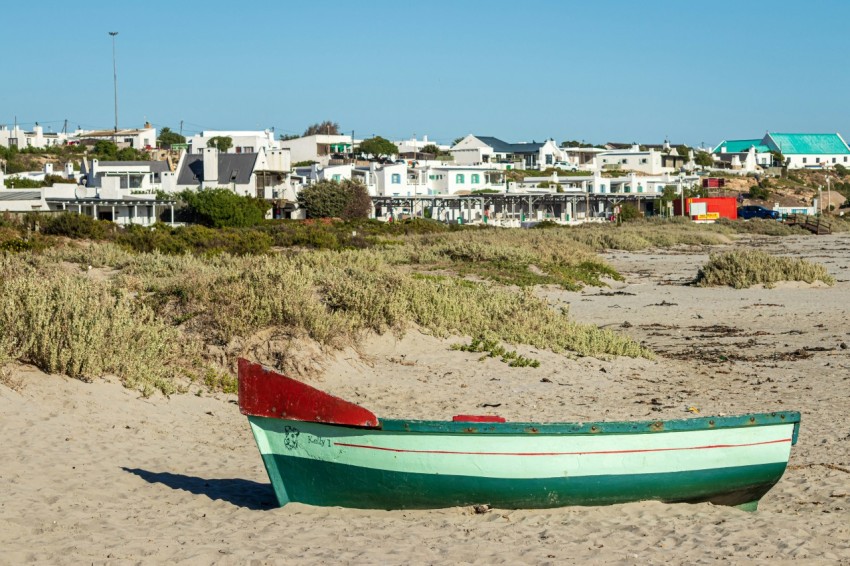 a green and red boat sitting on top of a sandy beach