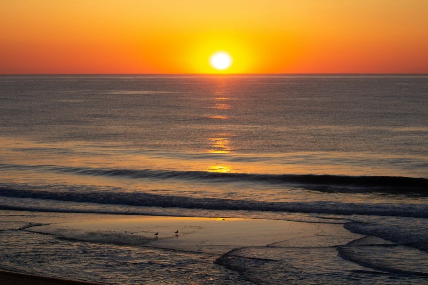 the sun is setting over the ocean on the beach