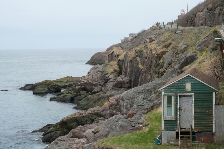 a small green house sitting on the side of a cliff next to the ocean