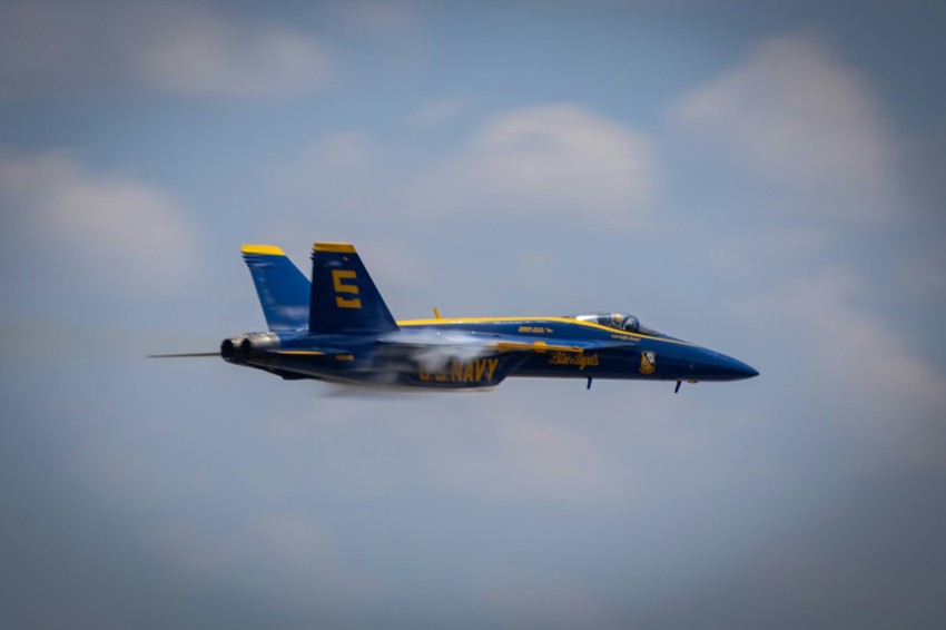 a blue and yellow jet flying through a cloudy sky