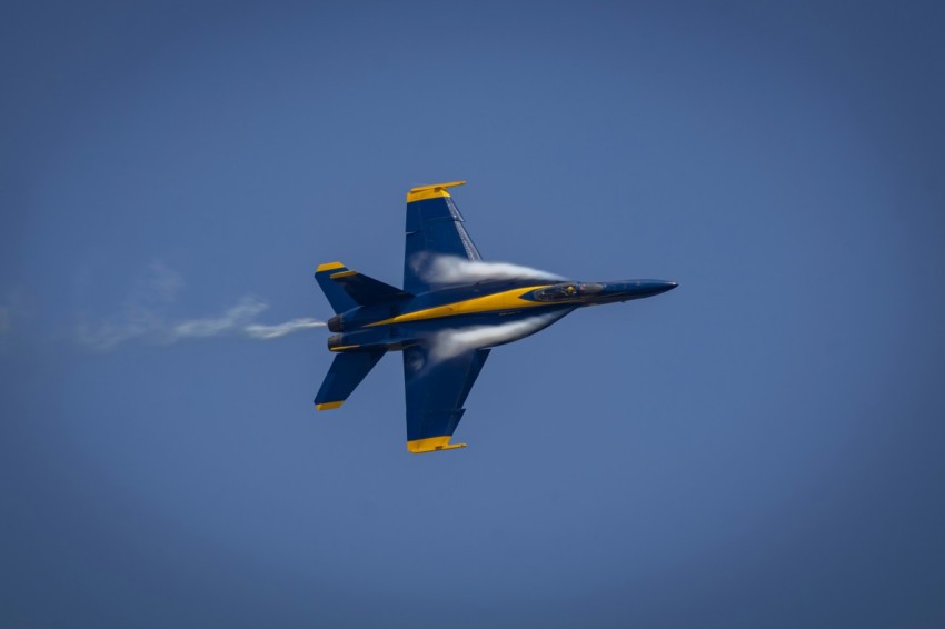 a blue and yellow jet flying through a blue sky