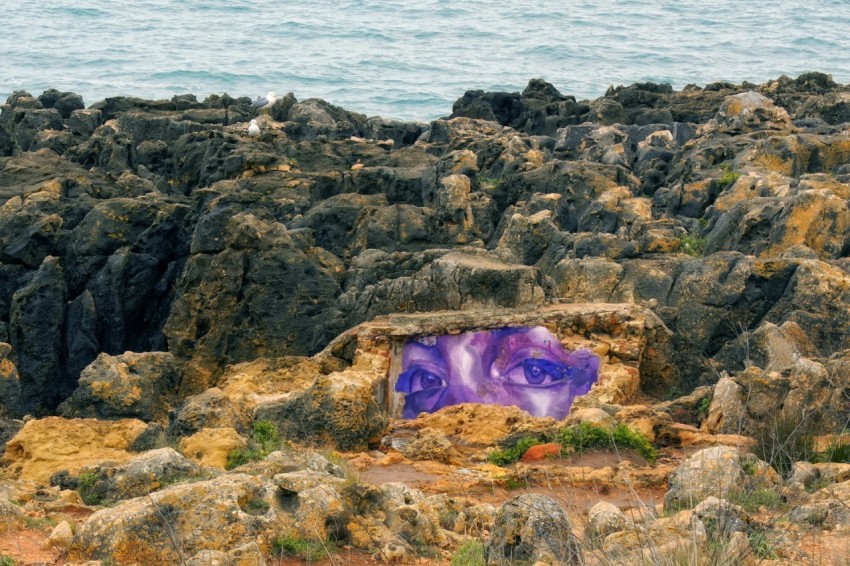 a purple piece of art sitting on top of a rocky beach gQGF4zG