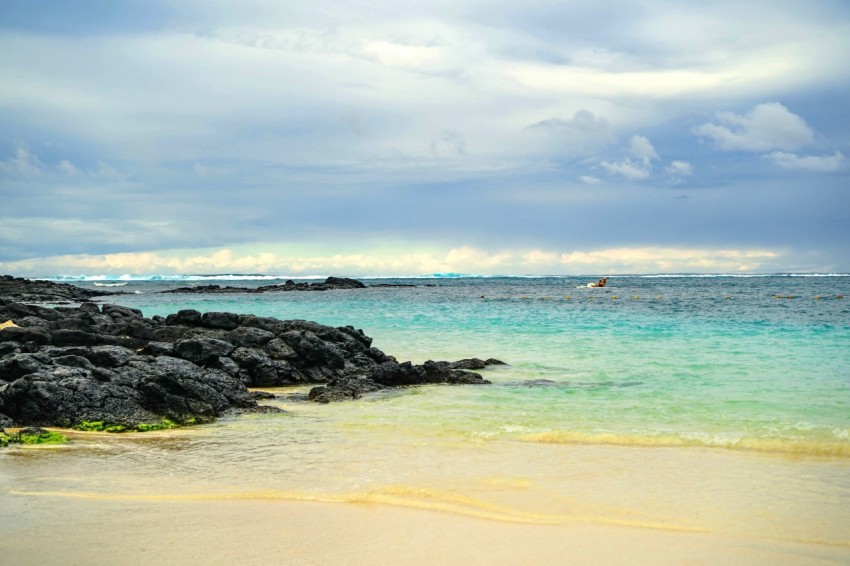 a sandy beach with blue water and rocks lm5