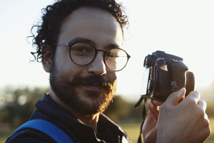 man wearing eyeglasses holding dslr camera