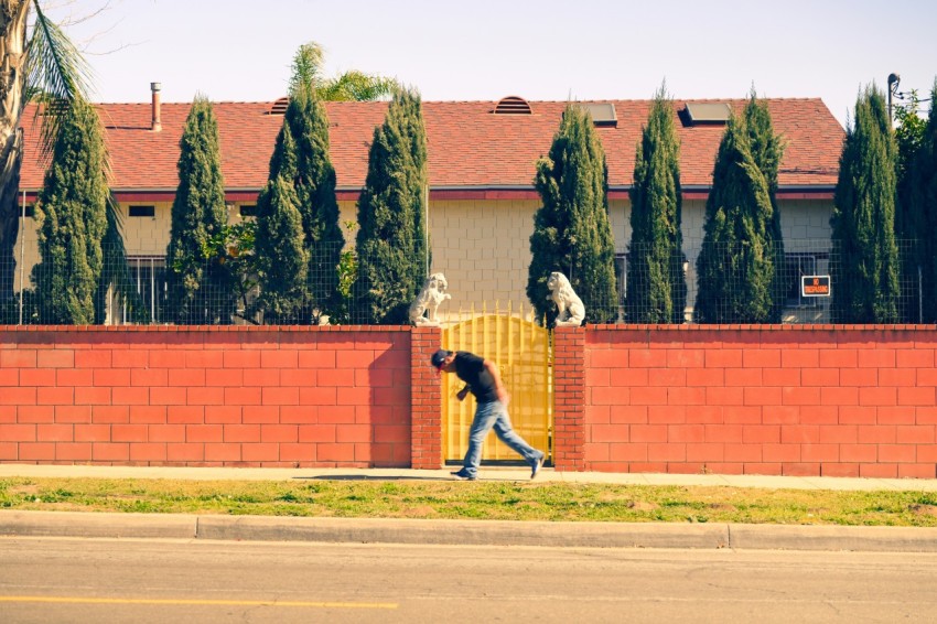 a man walking down a street past a red brick fence