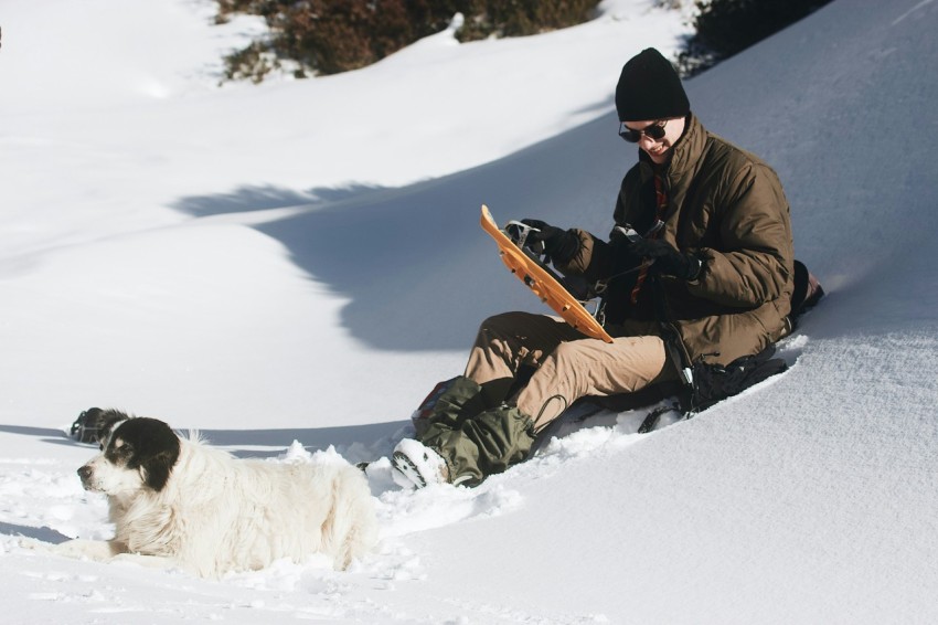 man in brown jacket and black pants sitting on snow covered ground during daytime