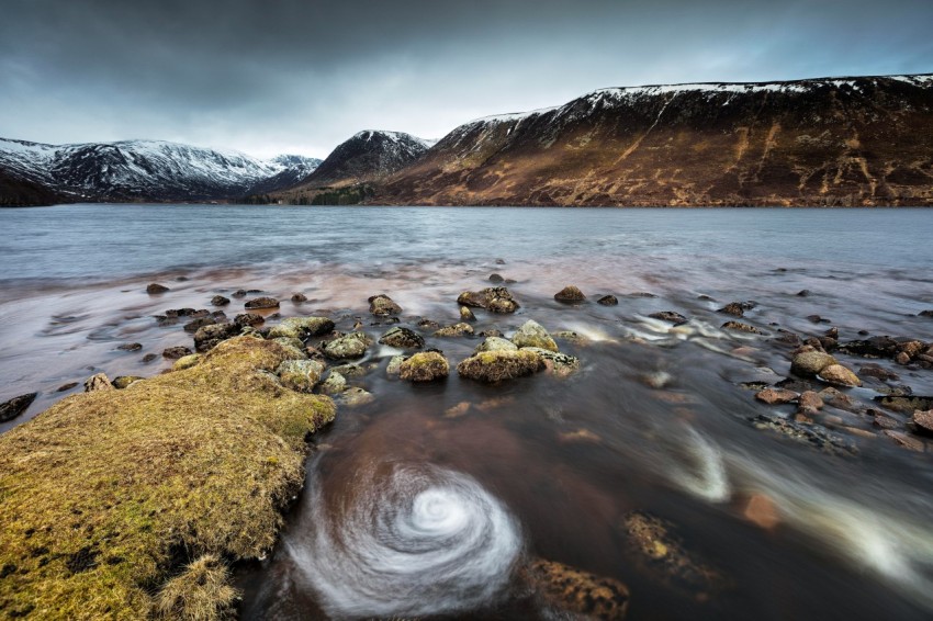 a rocky beach with a body of water and mountains in the background 2aj3yrhd