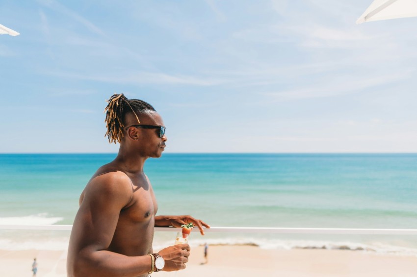 topless man wearing sunglasses standing near seashore nt