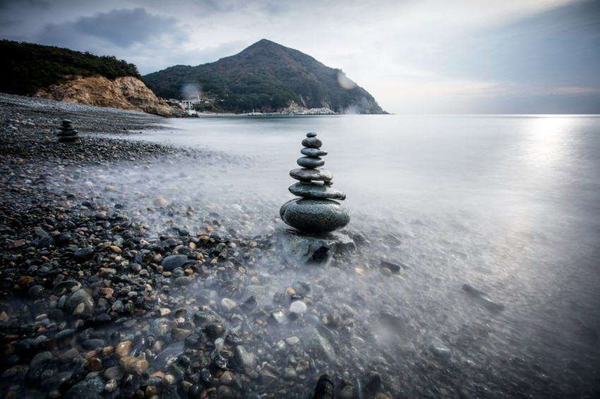 a rocky beach with a large stack of rocks in the water