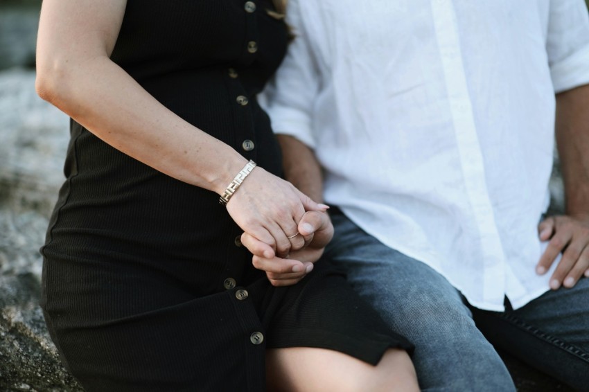 a man and woman holding hands while sitting on a rock