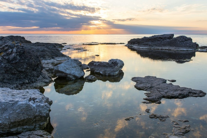 rocks on body of water under cloudy sky