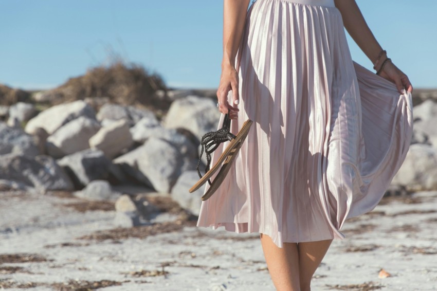 woman wearing white skirt holding black leather flat sandals standing