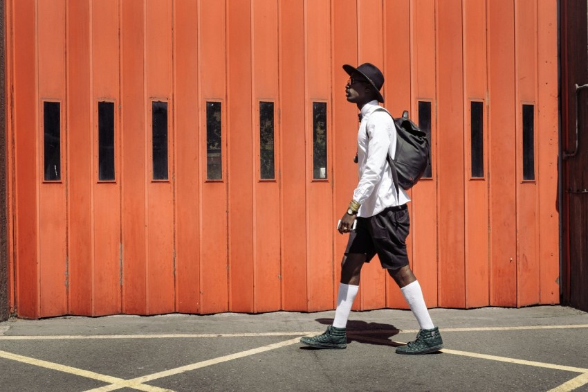 man wearing black hat and white dress shirt walking on street near orange gate