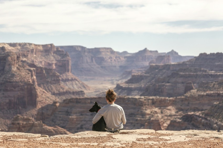 person with dog sitting on grand canyon cliff