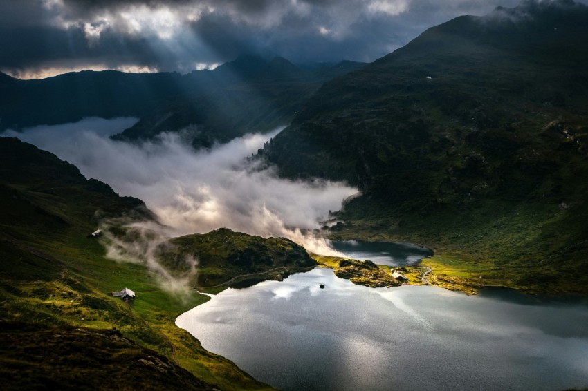 a lake surrounded by mountains under a cloudy sky