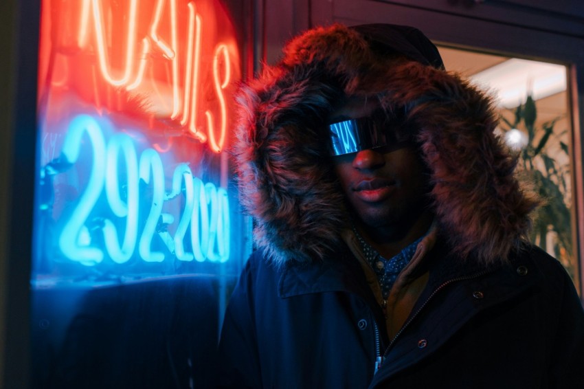 man in black full zip hoodie leaning on neon light signage