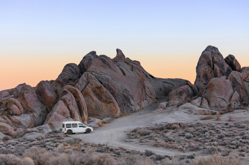 white car on gray sand near brown rock formation during daytime