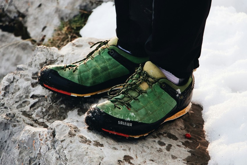 person in green black low top sneakers standing on top of rock