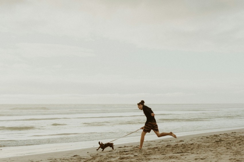 man in black shorts walking on beach with dog during daytime THI