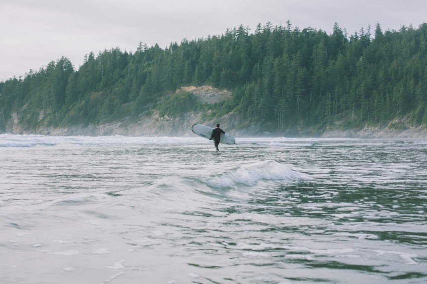 person walking on shore while holding surfboard during daytime