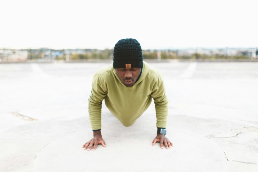 man in green long sleeved shirt doing a push up on gray concrete pavement