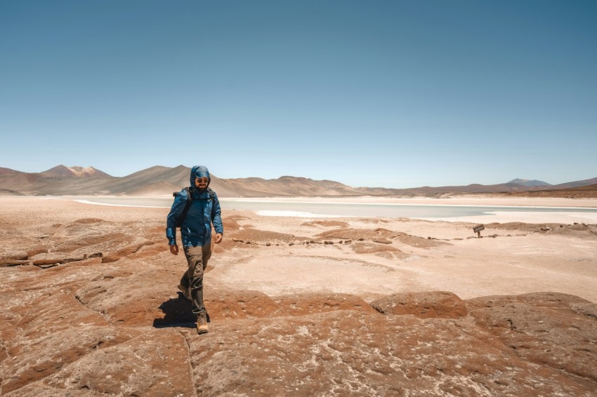 a man in a blue jacket walking across a desert