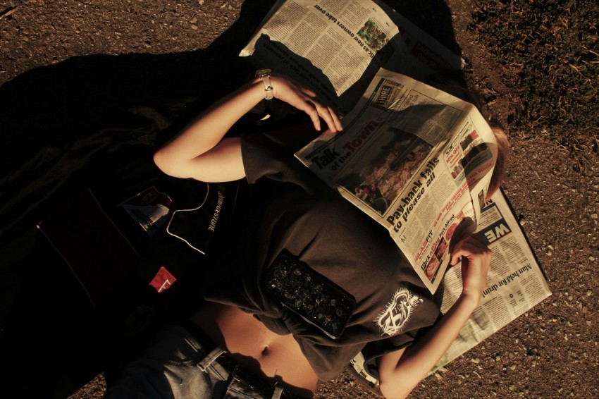 woman in black t shirt and black shorts sitting on ground reading newspaper