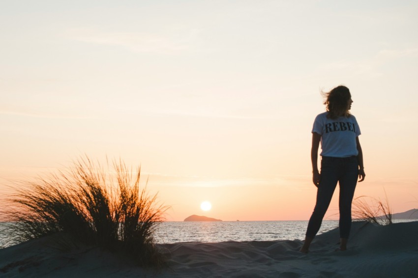 woman in blue t shirt standing on seashore during sunset