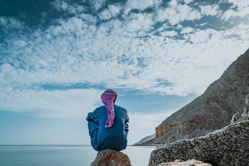 man wearing teal thobe robe sitting on rock