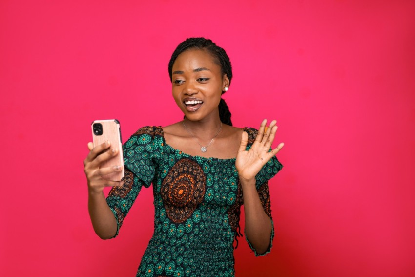 a woman holding a cell phone in front of a pink background Sl