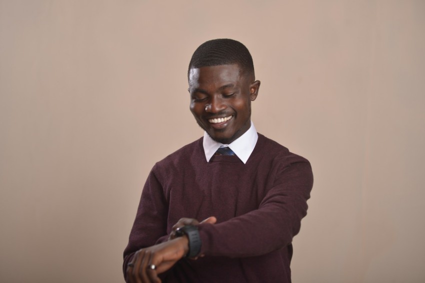 a man in a sweater and tie smiles while looking at his watch